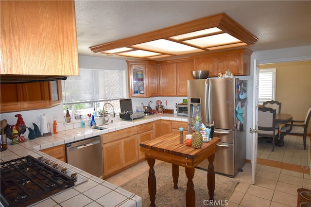 kitchen with tile counters, appliances with stainless steel finishes, light tile patterned floors, and sink