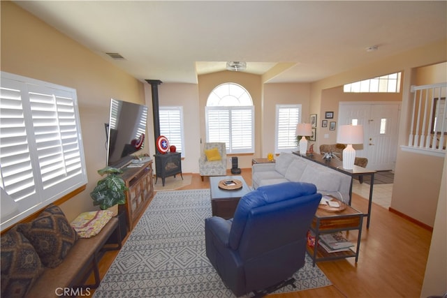 living room with light hardwood / wood-style floors, vaulted ceiling, and a wood stove