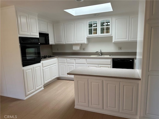 kitchen featuring sink, white cabinetry, a skylight, light wood-type flooring, and black appliances