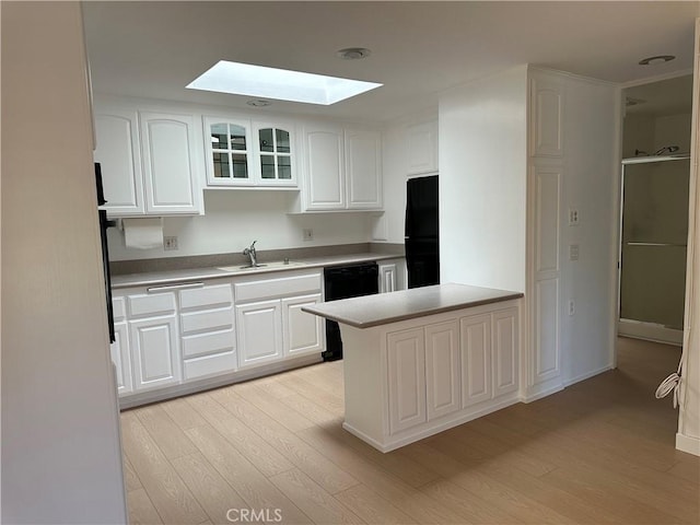 kitchen with a skylight, sink, white cabinets, black appliances, and light wood-type flooring