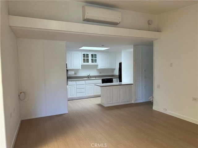 kitchen with sink, light hardwood / wood-style flooring, dishwasher, white cabinetry, and a wall unit AC