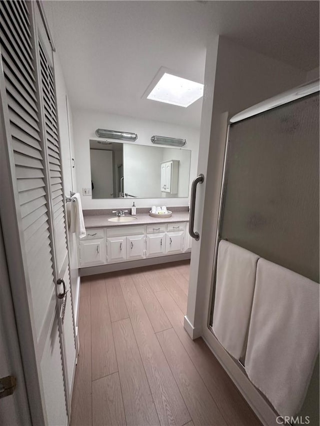 bathroom with vanity, a skylight, wood-type flooring, and a shower with shower door