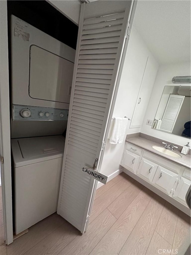 laundry area featuring stacked washer and dryer, sink, and light hardwood / wood-style floors