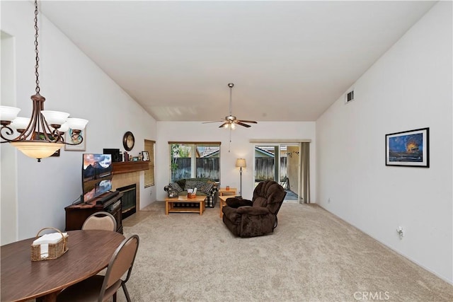 living room with ceiling fan with notable chandelier, carpet floors, and a tile fireplace