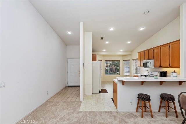 kitchen with kitchen peninsula, vaulted ceiling, white appliances, light carpet, and a breakfast bar