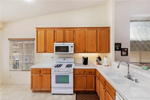 kitchen with tile counters, lofted ceiling, white appliances, and sink