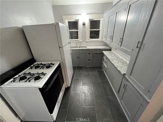 kitchen with white range with gas stovetop, sink, light stone counters, gray cabinets, and decorative backsplash