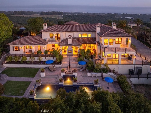 back house at dusk featuring a balcony, a patio, and an outdoor fire pit