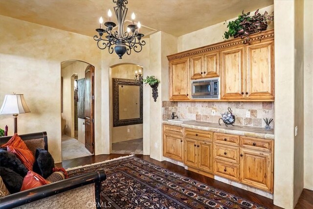 kitchen with light stone countertops, stainless steel microwave, a notable chandelier, backsplash, and decorative light fixtures