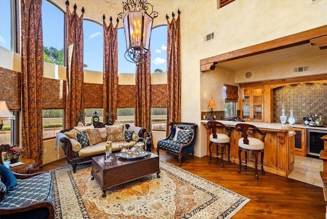 living room with a high ceiling, indoor bar, a notable chandelier, dark hardwood / wood-style flooring, and beverage cooler