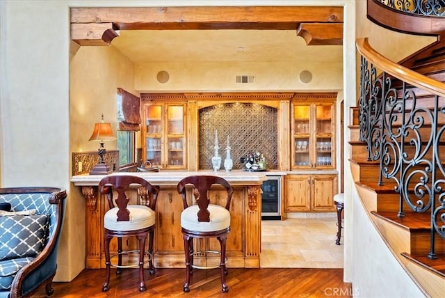 bar with beam ceiling, tasteful backsplash, light hardwood / wood-style flooring, and beverage cooler