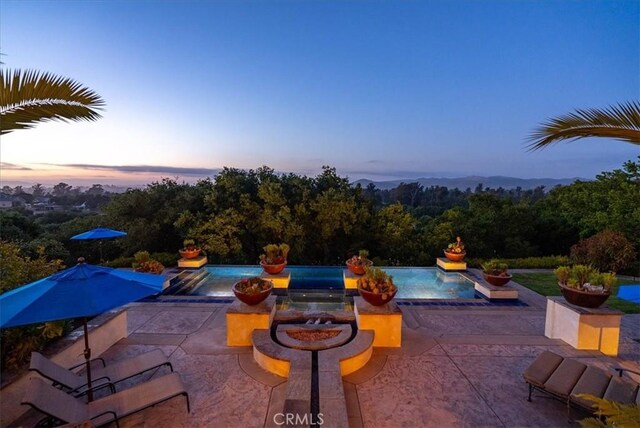 pool at dusk with a fire pit, a patio area, and an in ground hot tub