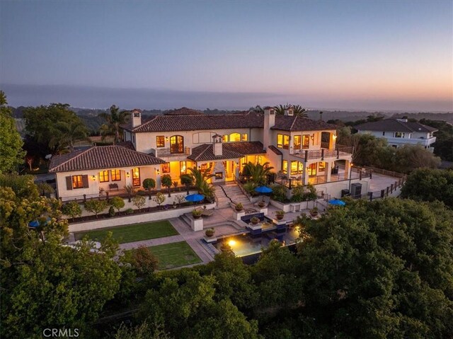 back house at dusk with a balcony and a patio