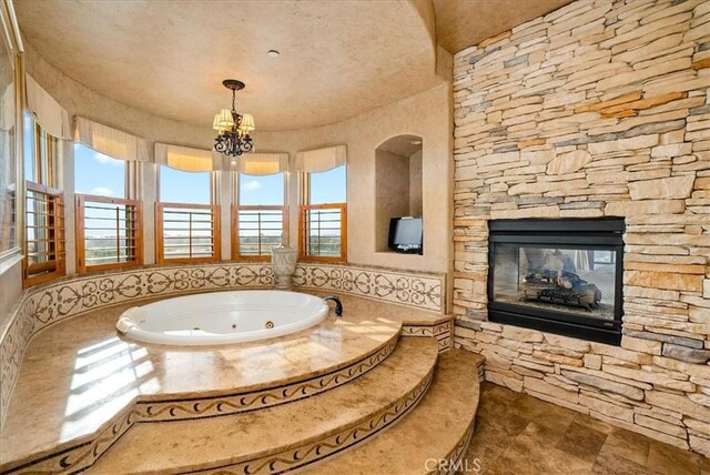 bathroom featuring a relaxing tiled tub, a multi sided fireplace, plenty of natural light, and an inviting chandelier