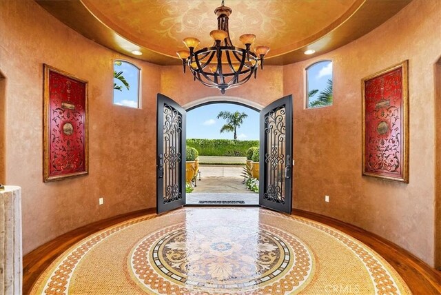 foyer entrance with an inviting chandelier, a raised ceiling, and french doors