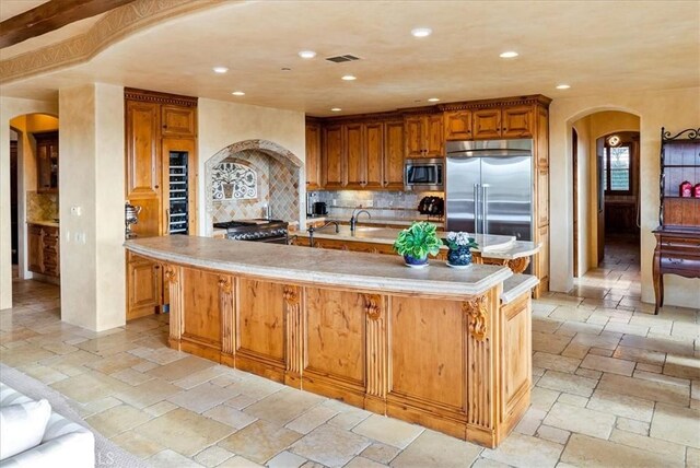 kitchen with built in appliances, decorative backsplash, and a large island with sink