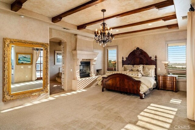 carpeted bedroom with multiple windows, a premium fireplace, beamed ceiling, and a notable chandelier