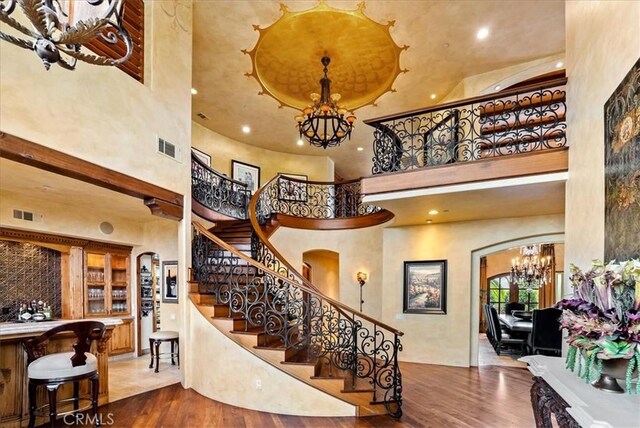 staircase with wood-type flooring, a towering ceiling, and a notable chandelier