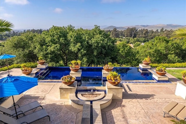 view of pool featuring an in ground hot tub, a mountain view, a patio, and a fire pit