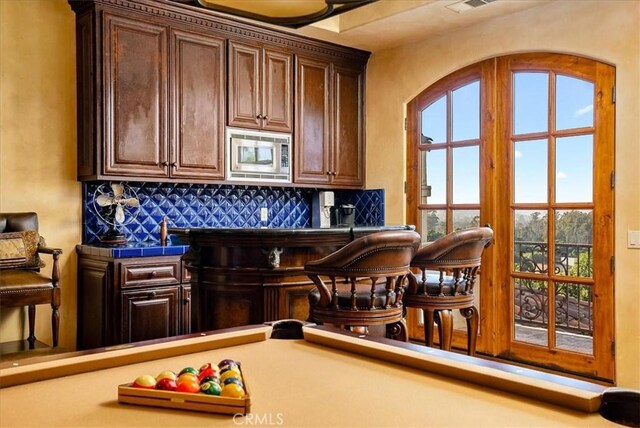 bar featuring dark brown cabinets, tasteful backsplash, stainless steel microwave, and pool table