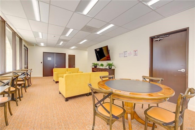 dining space with a drop ceiling and light colored carpet