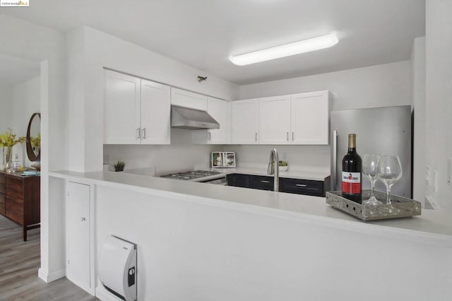 kitchen featuring sink, stainless steel stove, range hood, white cabinets, and light wood-type flooring