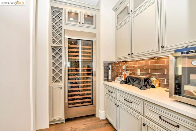 bar featuring tasteful backsplash, light hardwood / wood-style flooring, and beverage cooler