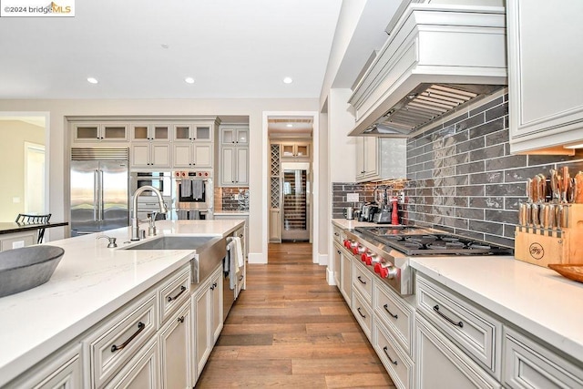 kitchen with sink, backsplash, light hardwood / wood-style floors, custom range hood, and appliances with stainless steel finishes