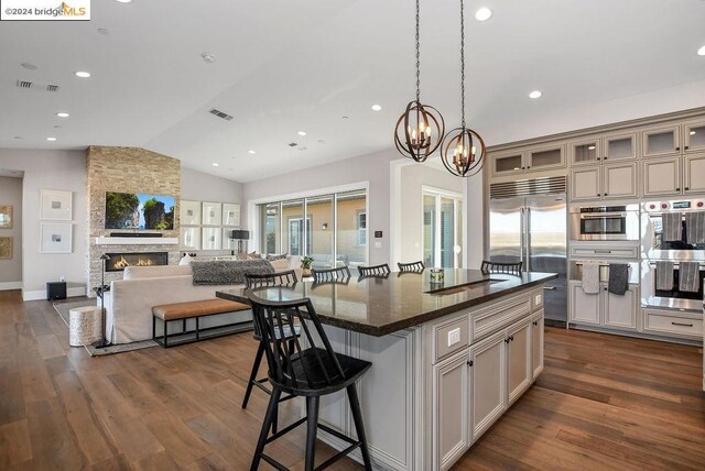 kitchen with stainless steel appliances, a kitchen island, dark stone countertops, a stone fireplace, and lofted ceiling