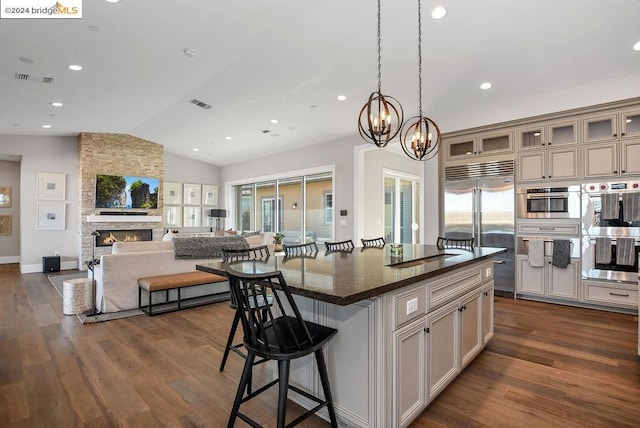 kitchen featuring dark stone counters, vaulted ceiling, a fireplace, a kitchen island, and appliances with stainless steel finishes