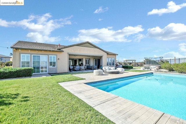 back of property with an outdoor hangout area, ceiling fan, a patio area, a fenced in pool, and a lawn