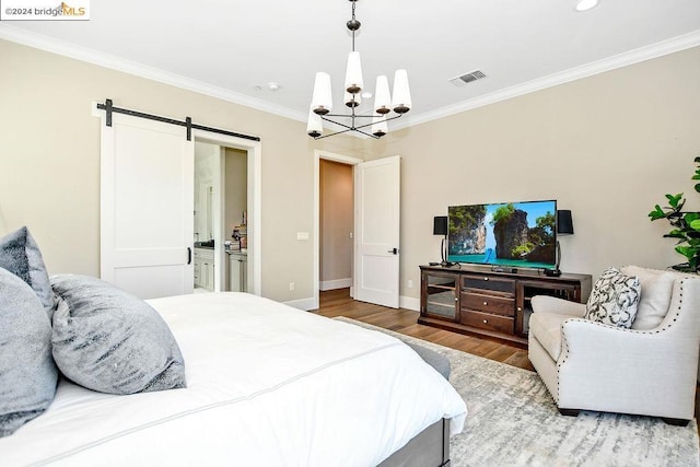 bedroom featuring ensuite bath, crown molding, a barn door, hardwood / wood-style flooring, and an inviting chandelier