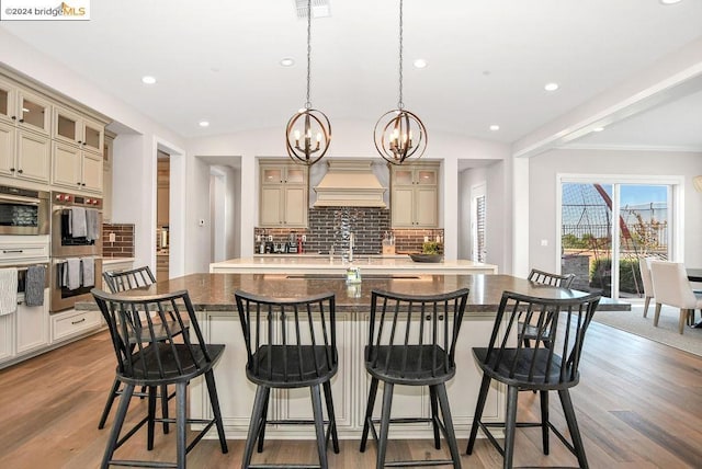 kitchen featuring premium range hood, cream cabinets, a kitchen breakfast bar, vaulted ceiling, and tasteful backsplash