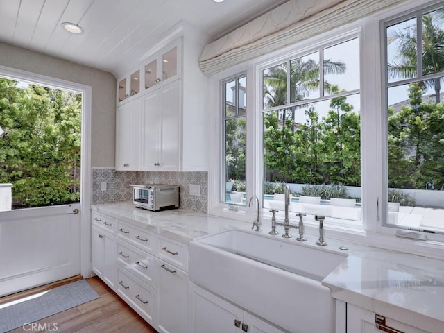 kitchen with backsplash, white cabinets, sink, light hardwood / wood-style flooring, and light stone countertops