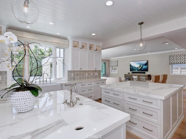 kitchen with backsplash, sink, light wood-type flooring, decorative light fixtures, and white cabinetry