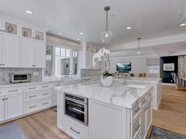 kitchen with sink, light hardwood / wood-style floors, white cabinetry, hanging light fixtures, and an island with sink