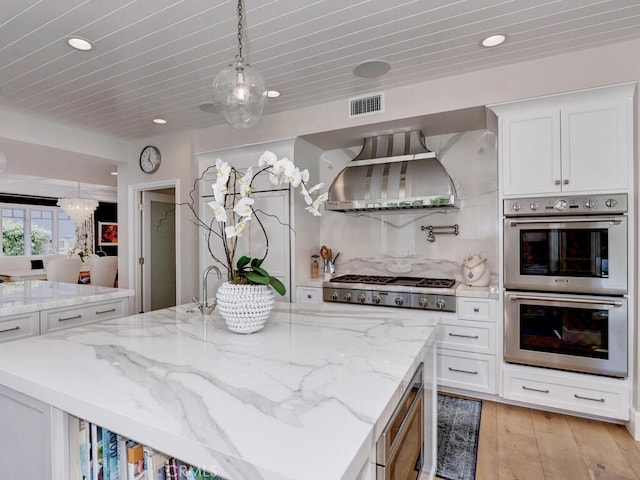 kitchen with appliances with stainless steel finishes, a kitchen island with sink, light hardwood / wood-style flooring, white cabinets, and range hood