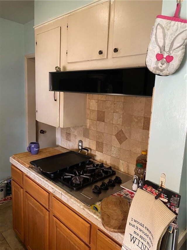 kitchen featuring tile patterned flooring, decorative backsplash, black gas stovetop, and ventilation hood