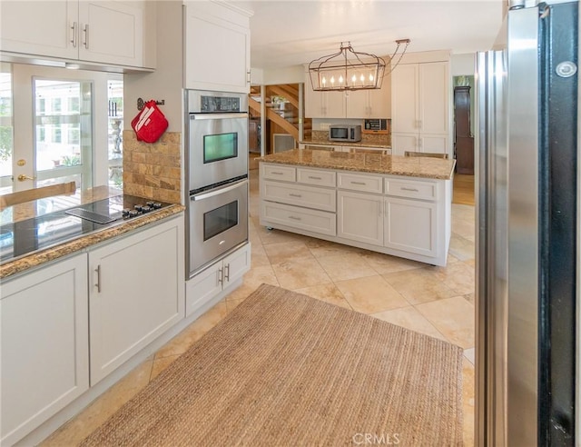 kitchen with backsplash, white cabinets, stainless steel appliances, and decorative light fixtures