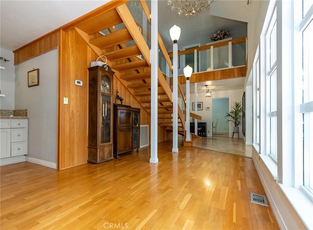 unfurnished living room with a chandelier, light wood-type flooring, ornate columns, and wood walls