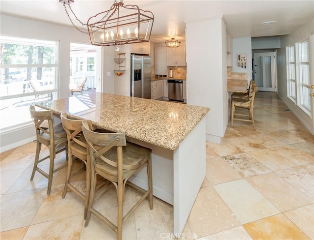 kitchen with an inviting chandelier, light stone counters, pendant lighting, a breakfast bar area, and appliances with stainless steel finishes