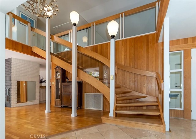 stairs featuring hardwood / wood-style flooring, decorative columns, wooden walls, and a notable chandelier