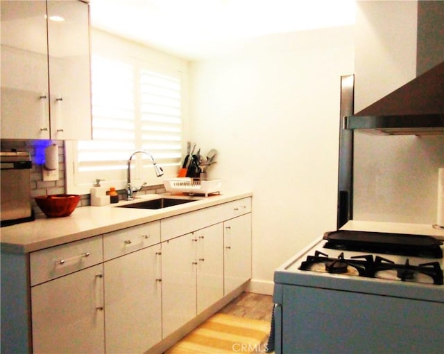 kitchen with ventilation hood, sink, light hardwood / wood-style flooring, gas range gas stove, and white cabinetry