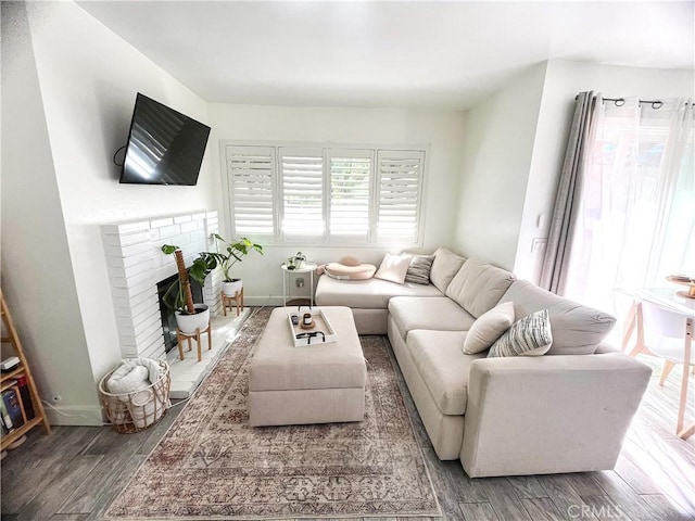 living area with baseboards, a brick fireplace, and wood finished floors