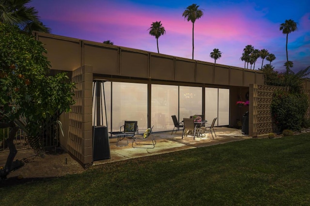 back house at dusk featuring a patio and a lawn