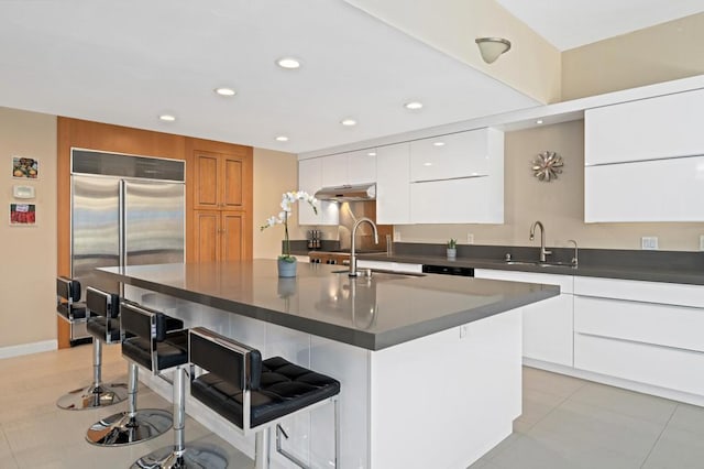 kitchen featuring stainless steel built in fridge, sink, an island with sink, a kitchen bar, and white cabinetry