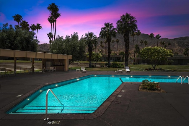 pool at dusk featuring a mountain view and a patio