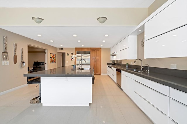 kitchen with a kitchen bar, stainless steel appliances, a kitchen island with sink, sink, and white cabinetry