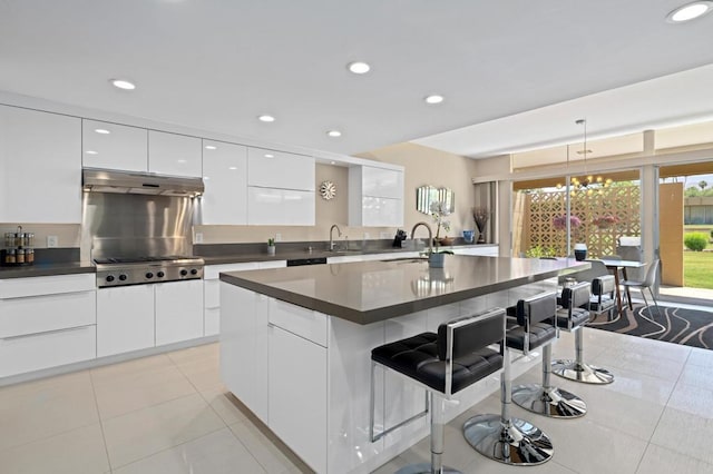 kitchen with a kitchen breakfast bar, stainless steel gas stovetop, white cabinets, hanging light fixtures, and an island with sink