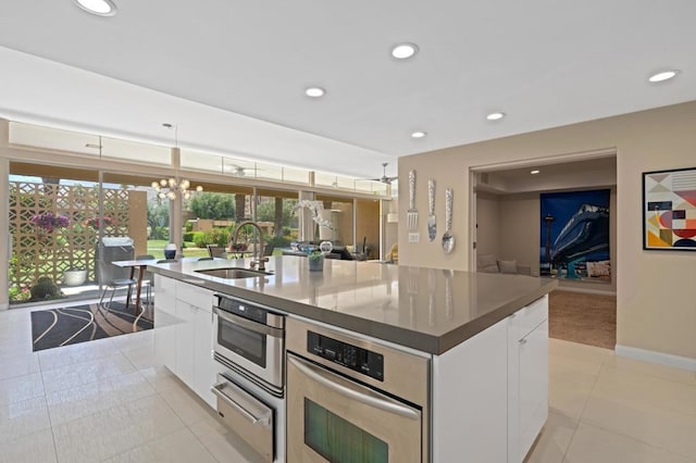 kitchen with stainless steel oven, a kitchen island with sink, sink, white cabinets, and hanging light fixtures